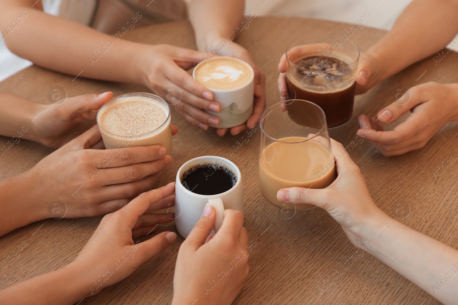 Photo of Friends drinking coffee at wooden table in cafe, closeup