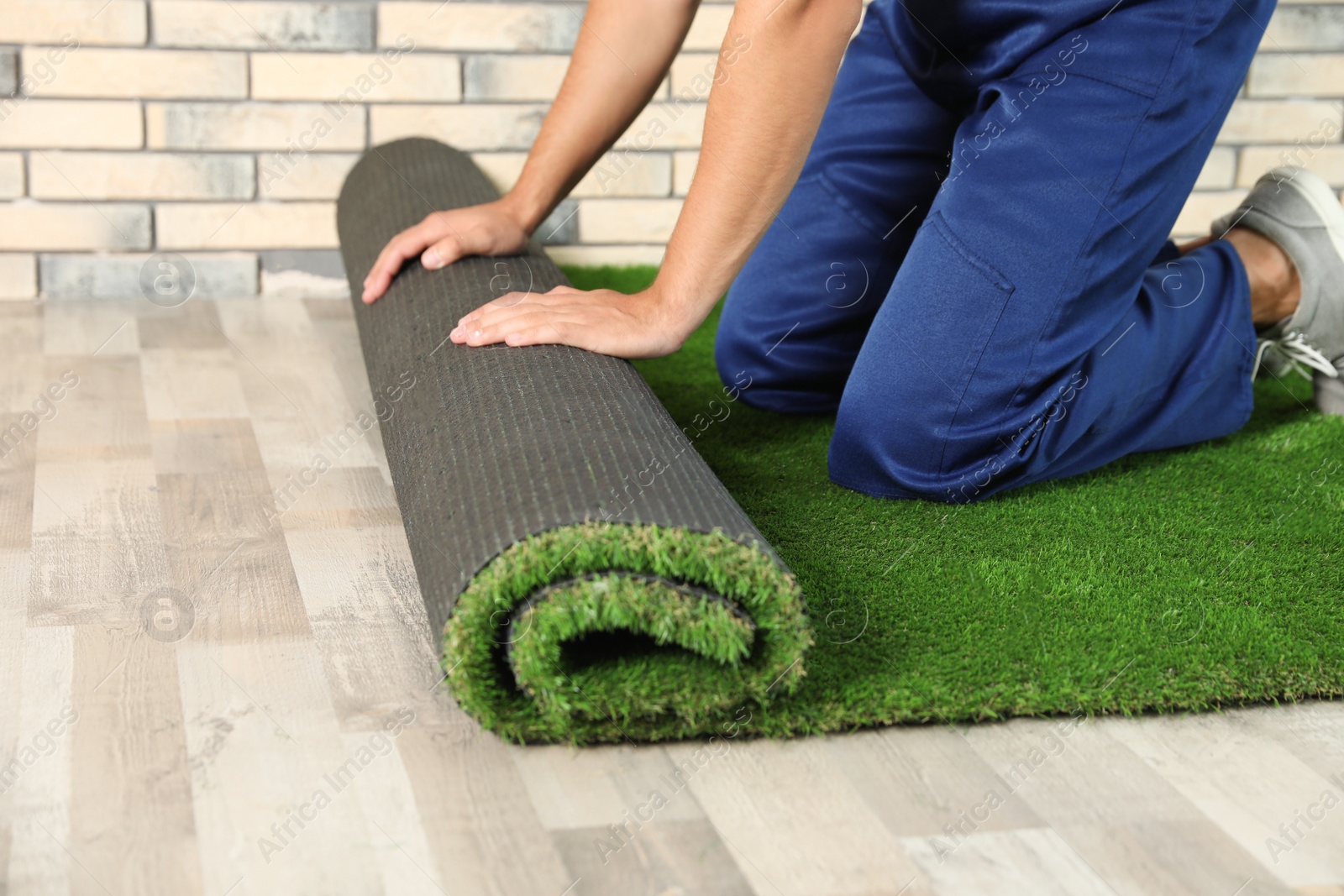 Photo of Man rolling out artificial grass carpet indoors, closeup