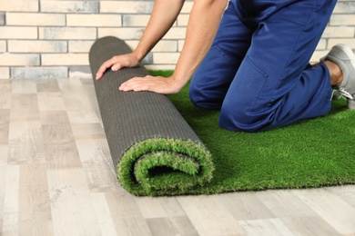 Man rolling out artificial grass carpet indoors, closeup