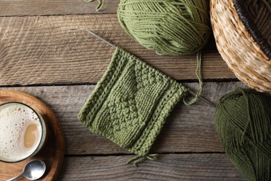 Photo of Soft green woolen yarn, knitting, needles and glass of drink on wooden table, flat lay