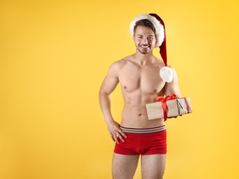 Photo of Shirtless sexy young Santa Claus with gift on color background