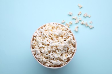 Paper bucket with delicious popcorn on light blue background, flat lay