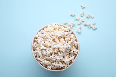 Photo of Paper bucket with delicious popcorn on light blue background, flat lay