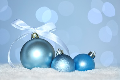 Beautiful light blue Christmas balls on snow against blurred festive lights