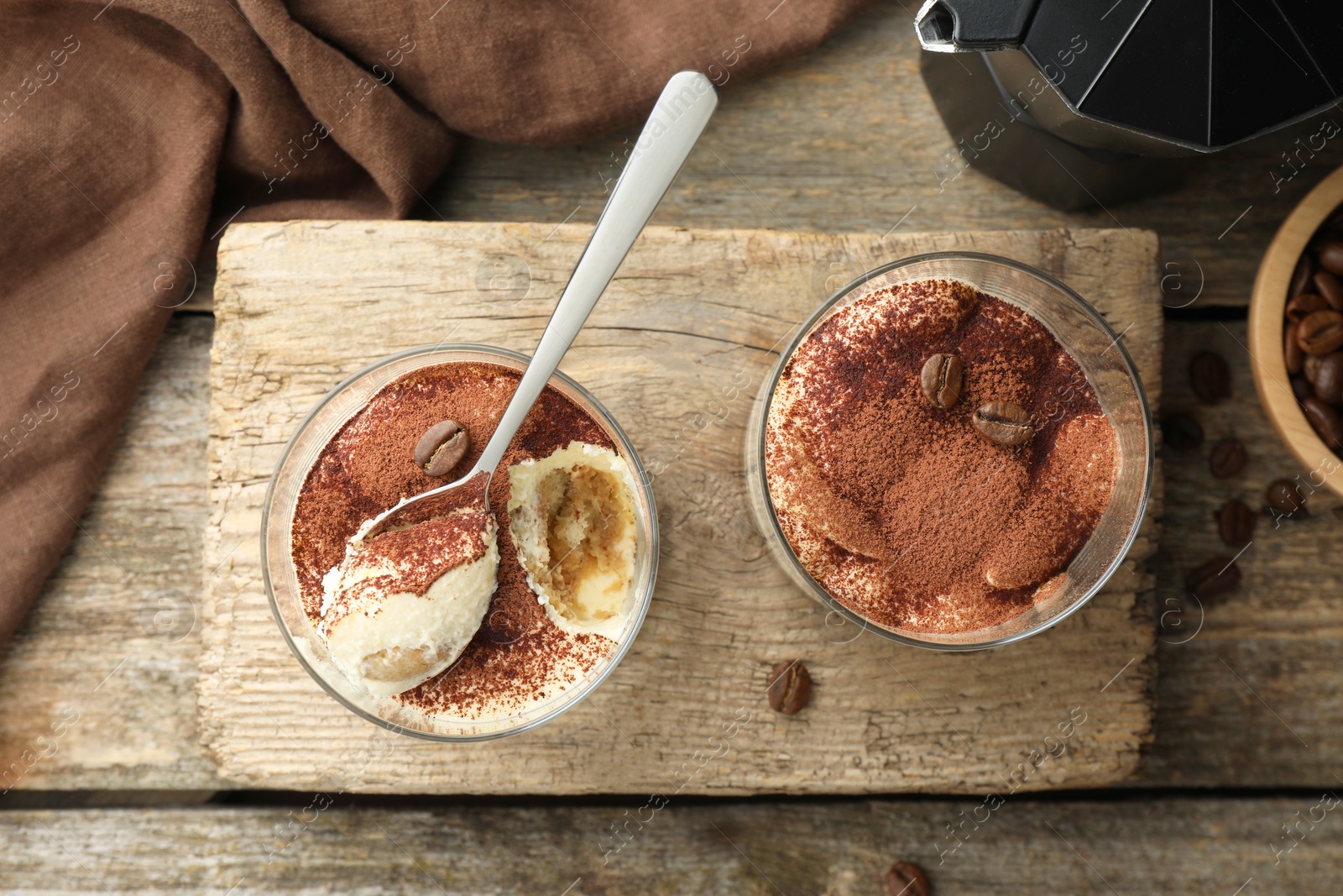 Photo of Delicious tiramisu in glasses, spoon and coffee beans on wooden table, top view