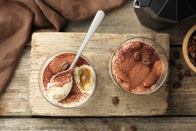 Photo of Delicious tiramisu in glasses, spoon and coffee beans on wooden table, top view