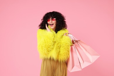 Happy young woman with shopping bags on pink background