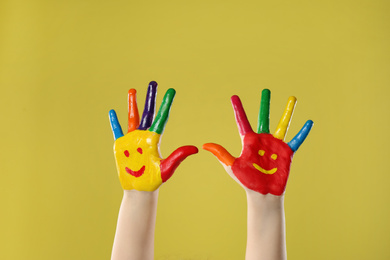 Photo of Kid with smiling faces drawn on palms against yellow background, closeup