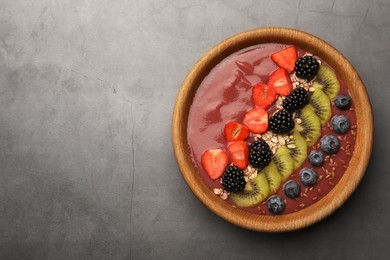 Bowl of delicious smoothie with fresh blueberries, strawberries, kiwi slices and blackberries on grey table, top view. Space for text
