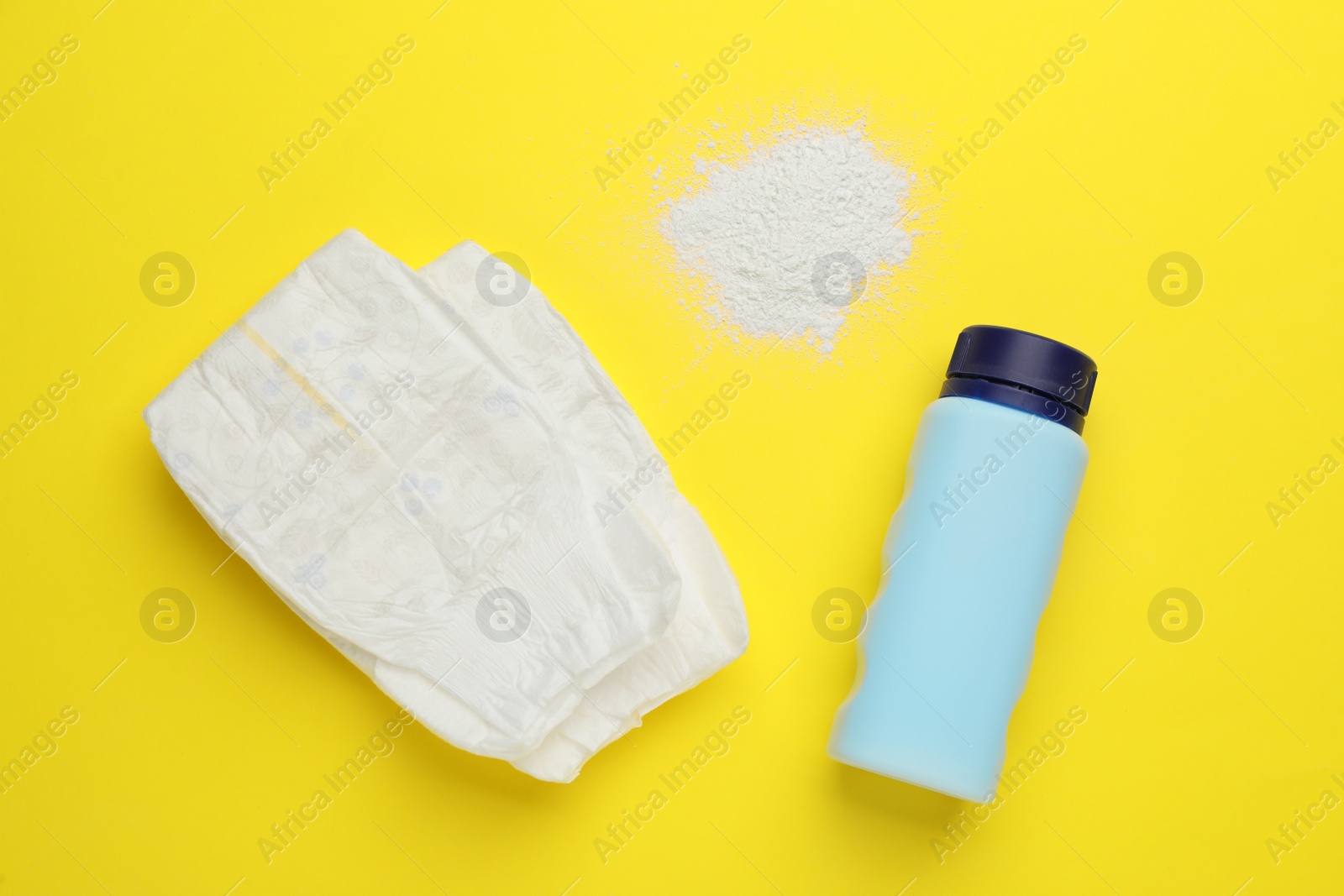 Photo of Dusting powder and diapers on yellow background, flat lay. Baby care products