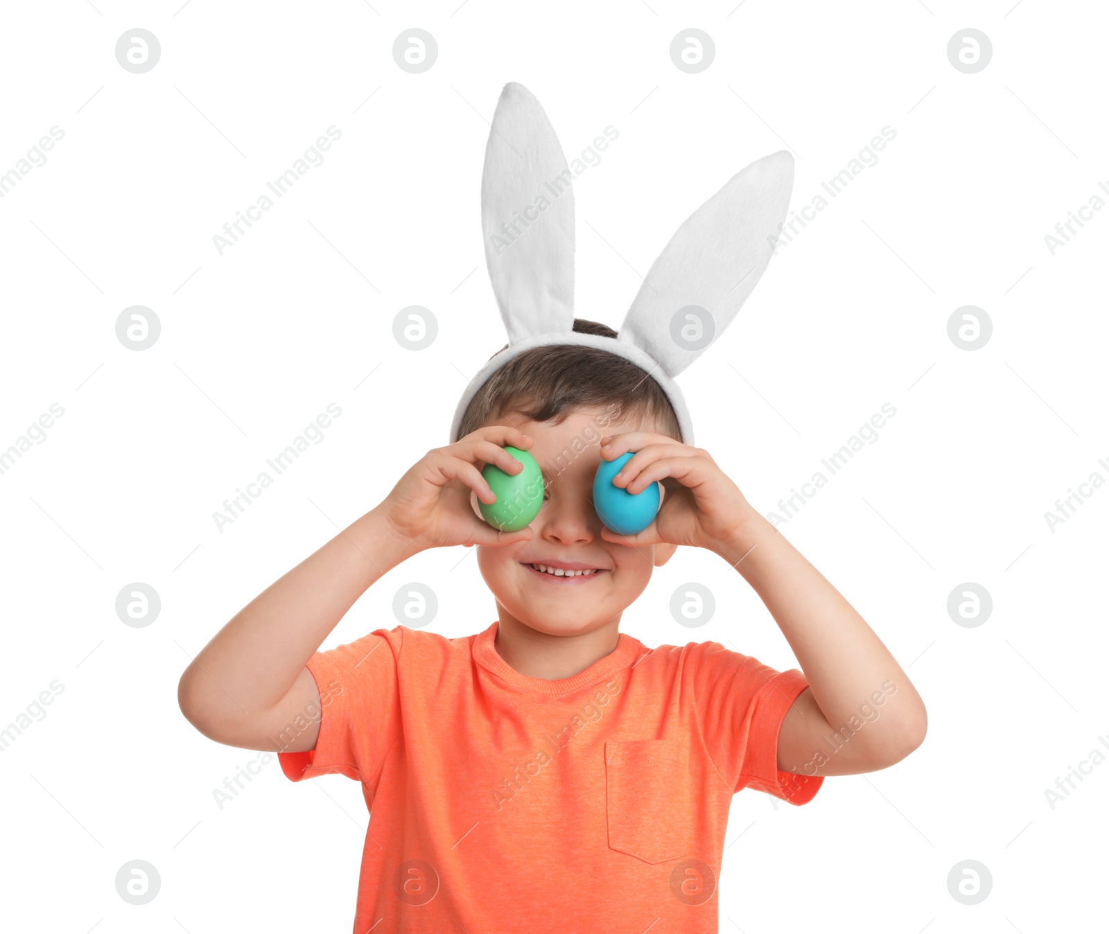 Photo of Little boy in bunny ears headband holding Easter eggs near eyes on white background