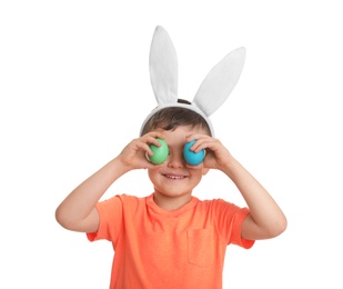 Photo of Little boy in bunny ears headband holding Easter eggs near eyes on white background