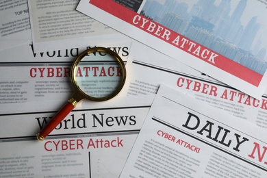 Newspaper with headline CYBER ATTACK and magnifying glass, top view