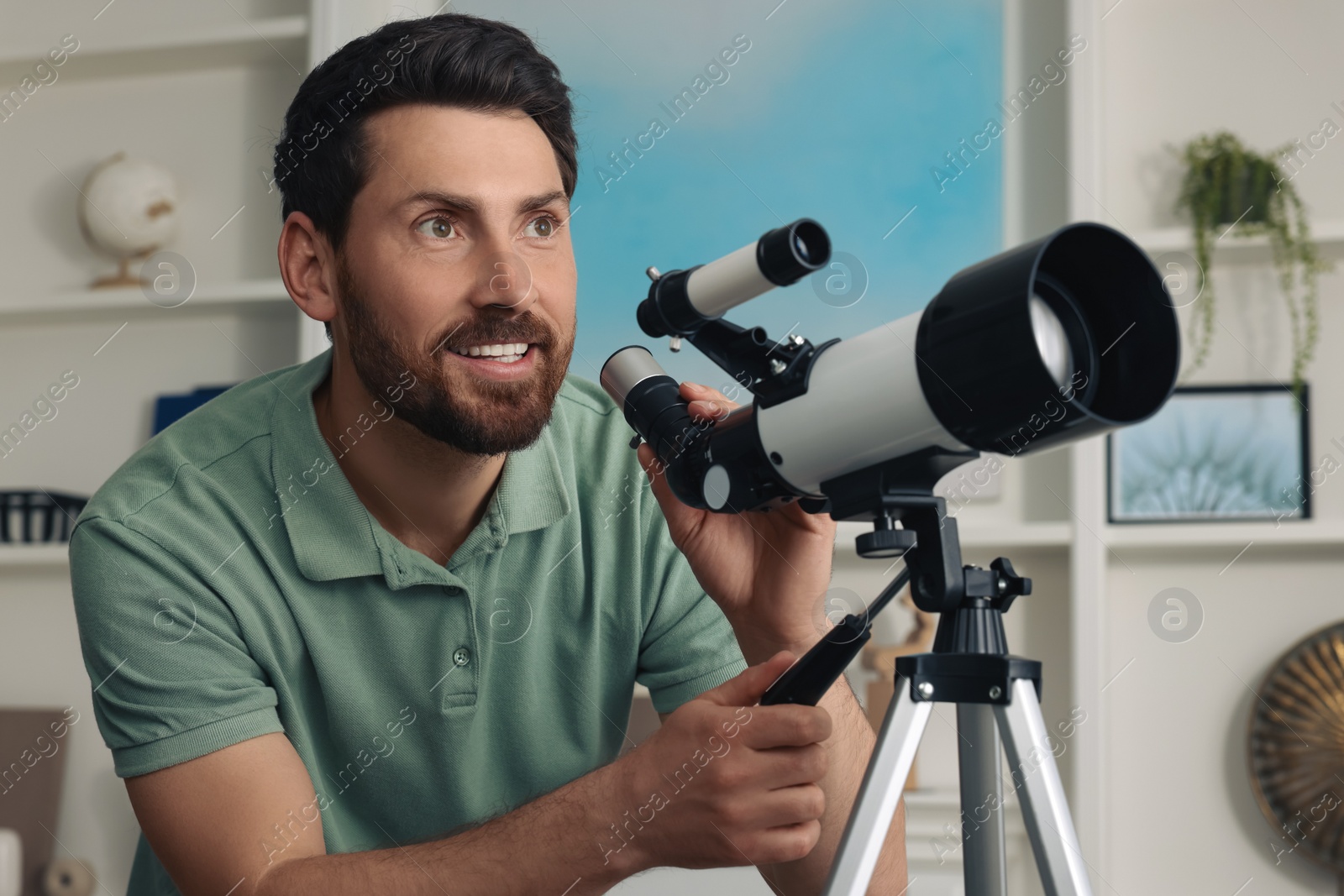 Photo of Handsome man using telescope to look at stars in room