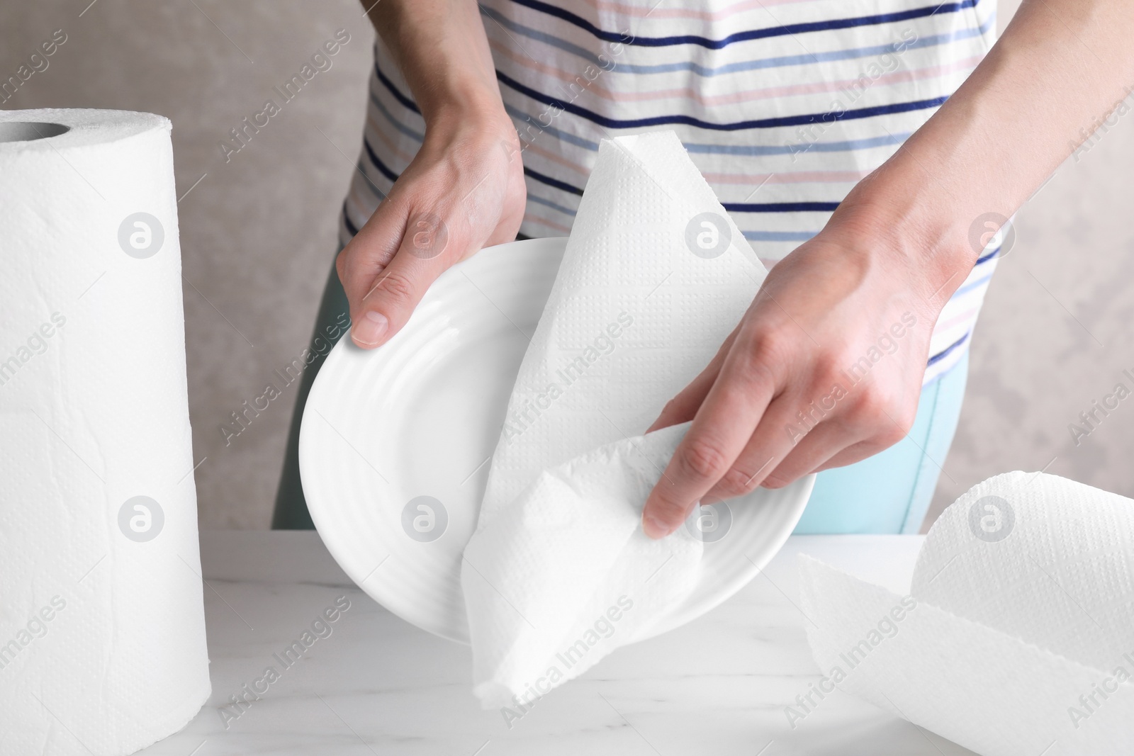 Photo of Woman wiping plate with tissue paper at white marble table, closeup