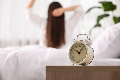 Photo of Alarm clock on nightstand. Woman awakening on bed at home, selective focus