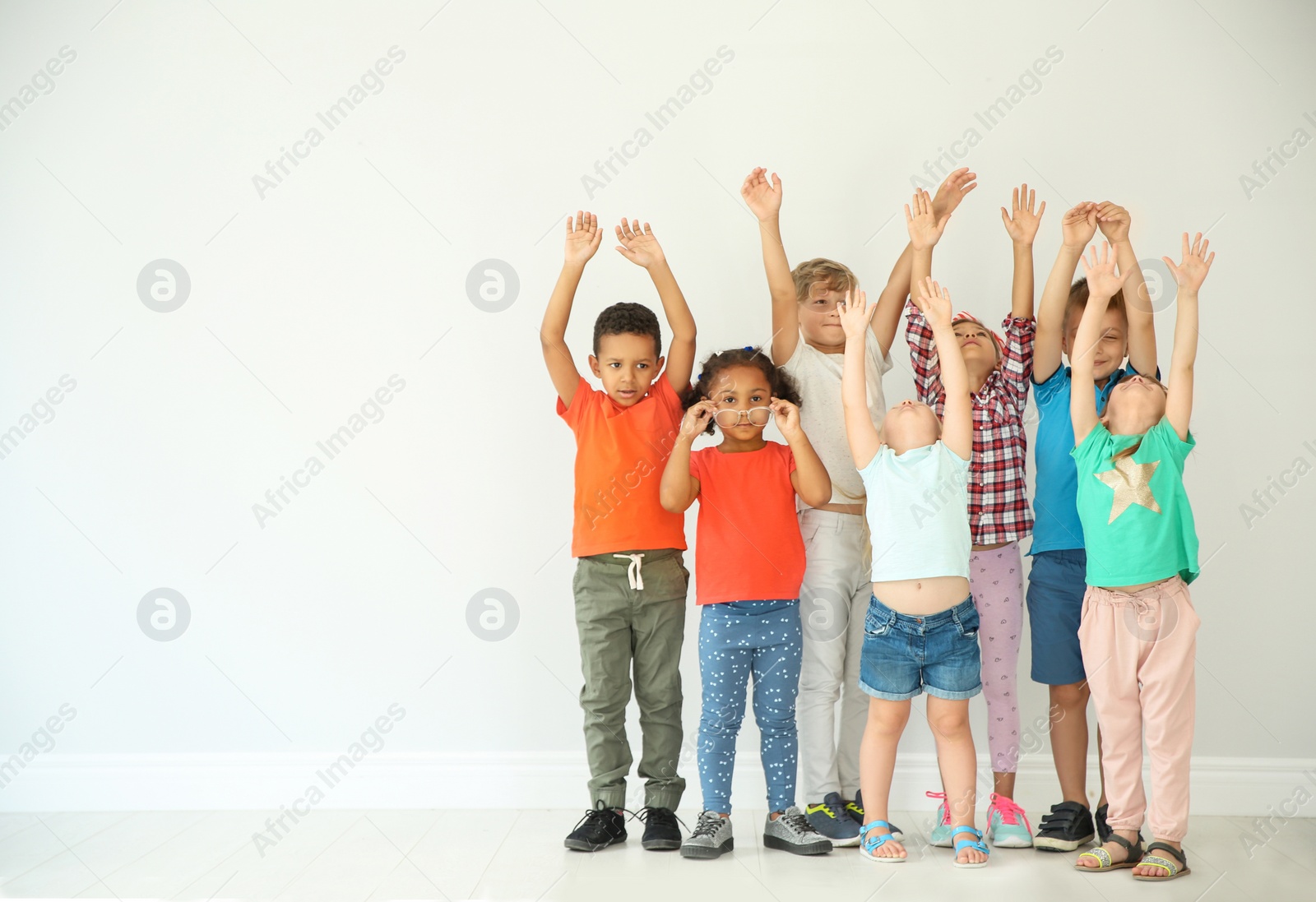 Photo of Little children raising hands together on light background. Unity concept