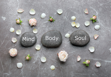 Photo of Stones with words MIND, BODY, SOUL and rose flowers on marble background, flat lay. Zen lifestyle