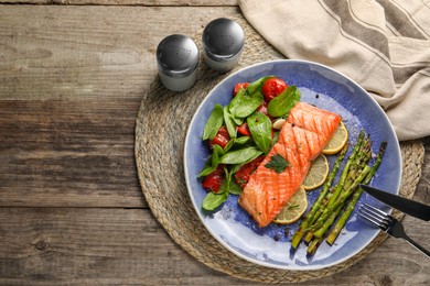 Photo of Tasty grilled salmon with tomatoes, asparagus, spinach and lemon served on wooden table, flat lay. Space for text