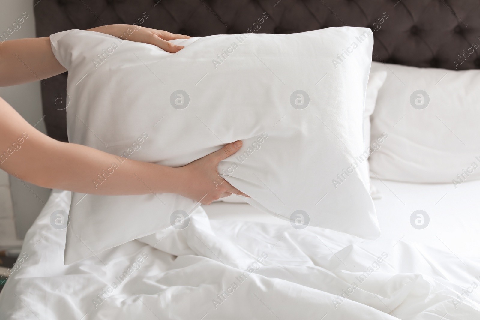 Photo of Young woman holding white pillow over bed, closeup