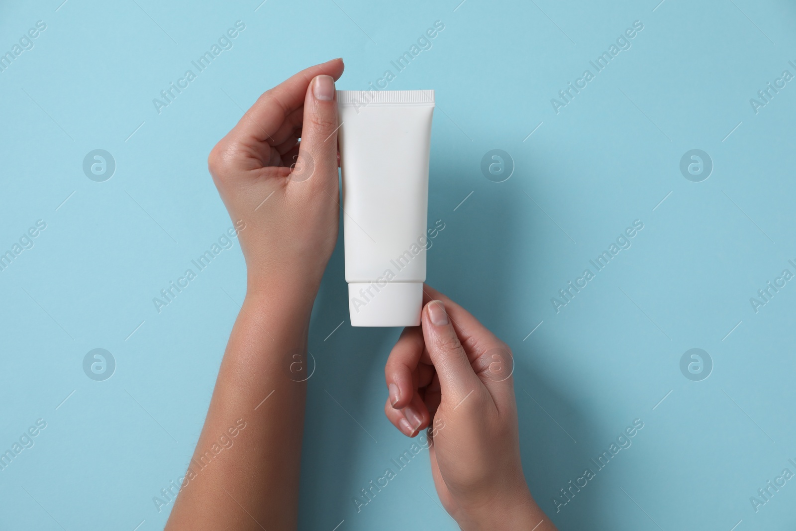 Photo of Woman with tube of hand cream on light blue background, top view