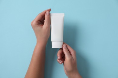 Woman with tube of hand cream on light blue background, top view