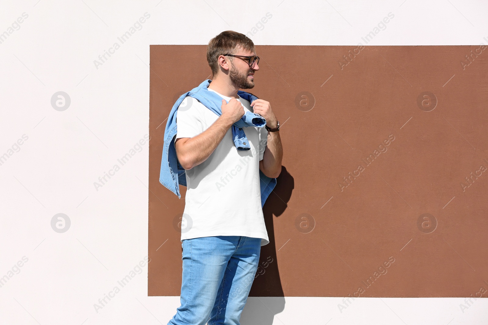 Photo of Young hipster man in stylish jeans posing near color wall