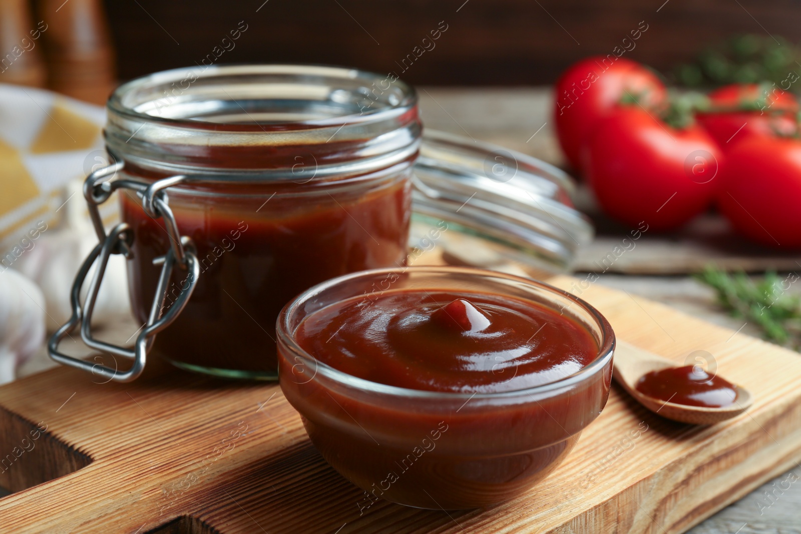 Photo of Tasty barbeque sauce in bowl, jar and spoon on table, closeup