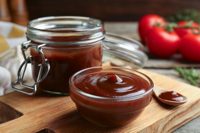 Tasty barbeque sauce in bowl, jar and spoon on table, closeup