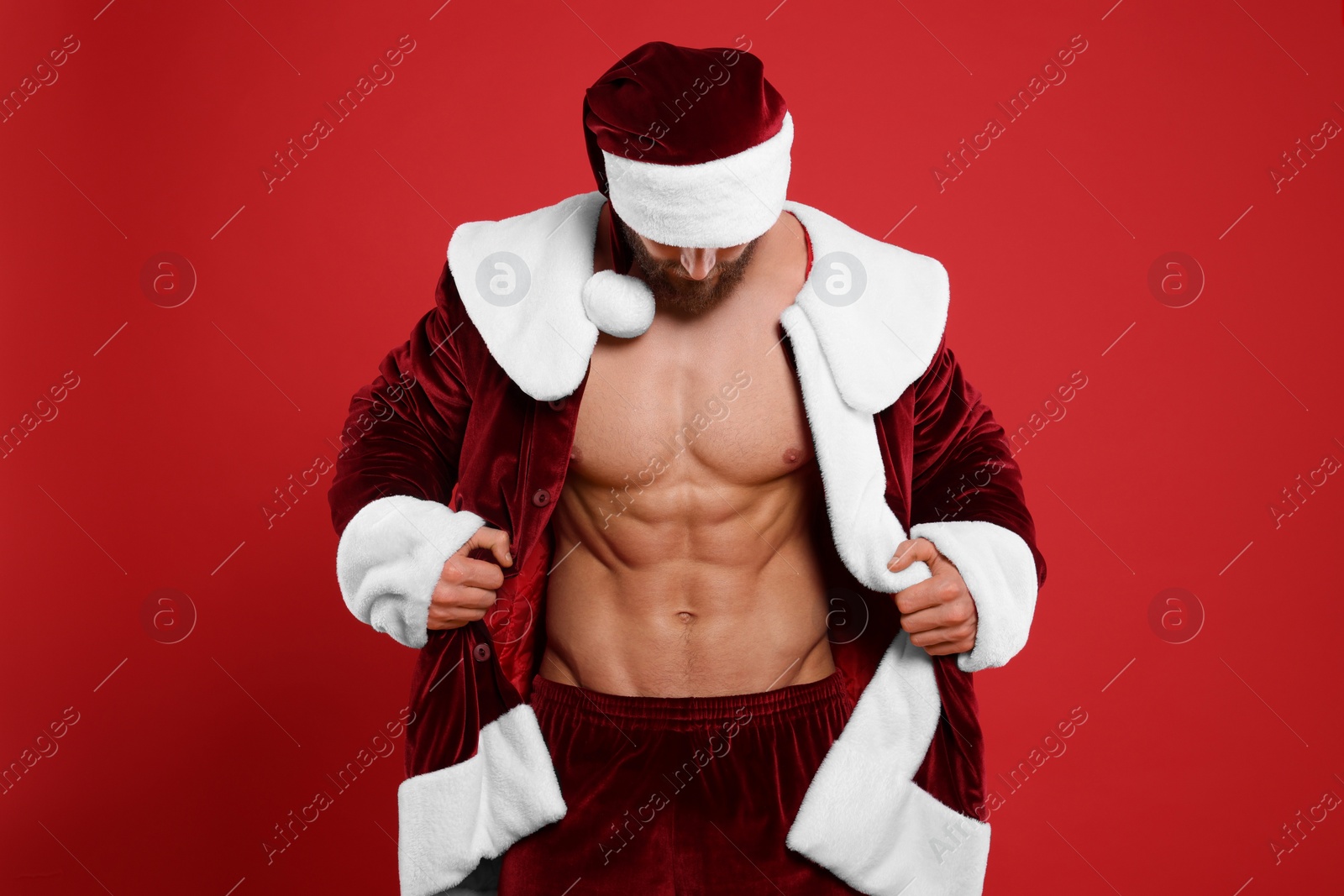 Photo of Attractive young man with muscular body in Santa costume on red background