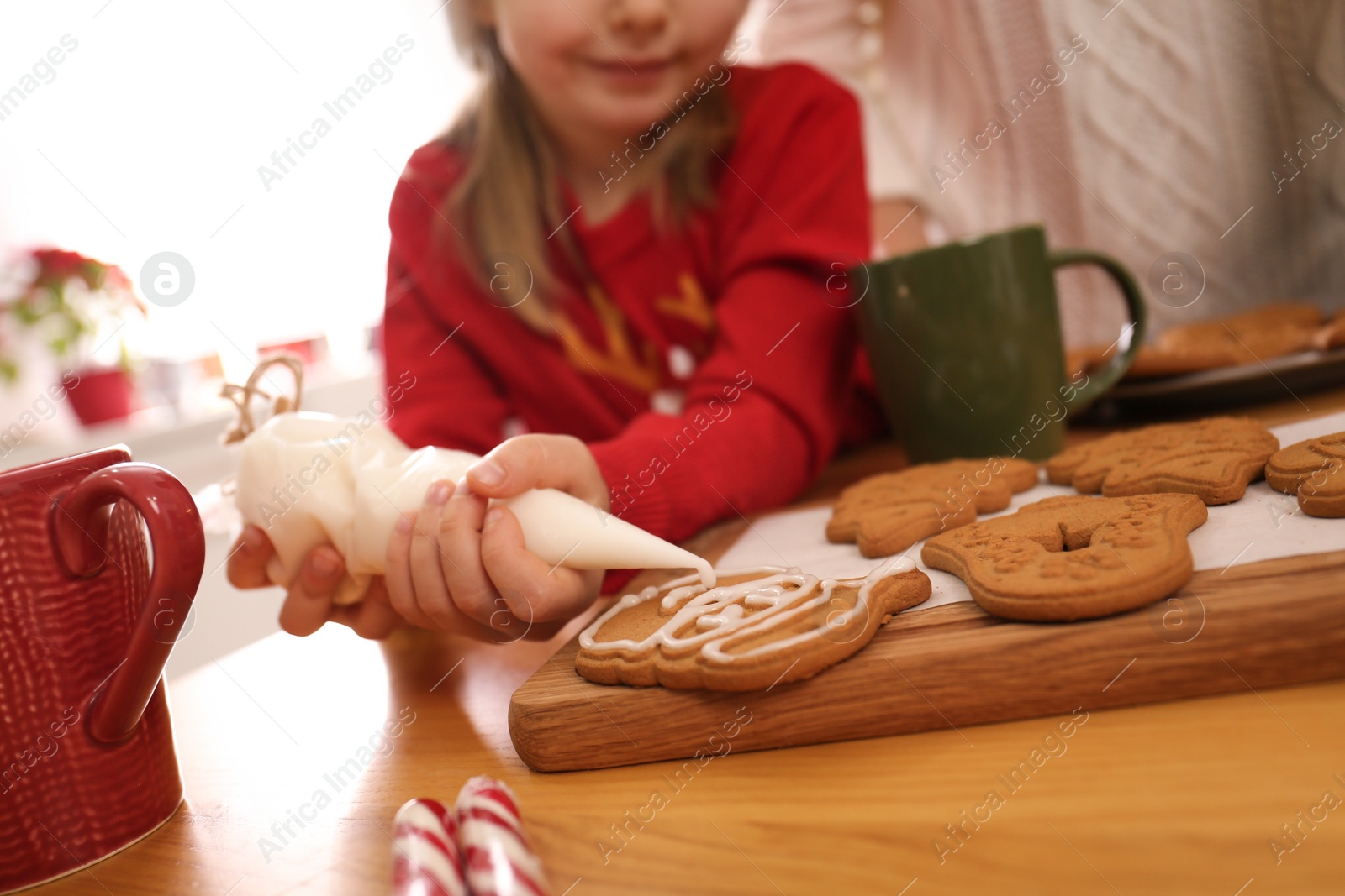 Photo of Little girl decorating tasty Christmas cookie at wooden table, closeup