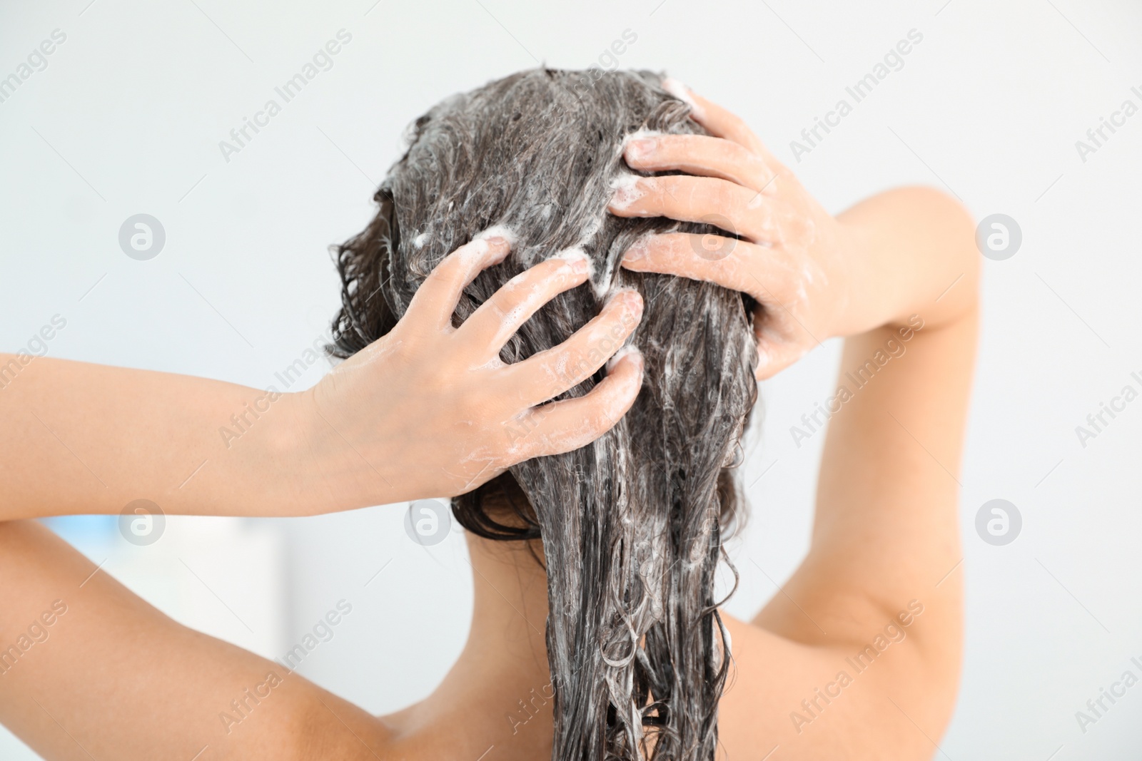 Photo of Woman applying shampoo onto her hair against light background