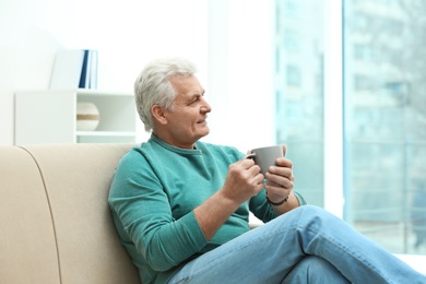 Portrait of mature man with cup of drink on sofa indoors