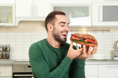 Young hungry man eating tasty sandwich in kitchen