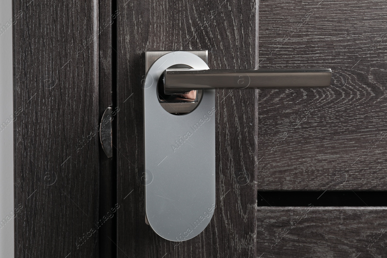 Photo of Closed wooden door with blank hanger on metal handle, closeup