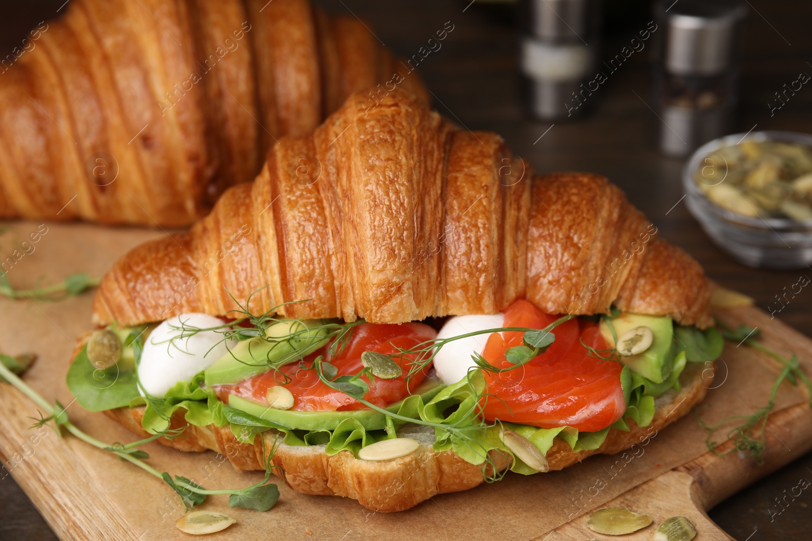 Photo of Tasty croissant with salmon, avocado, mozzarella and lettuce on wooden table, closeup