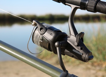 Photo of Fishing rod with reel at riverside, closeup