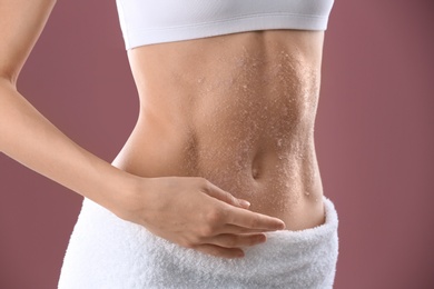 Young woman applying natural scrub on her belly against color background, closeup