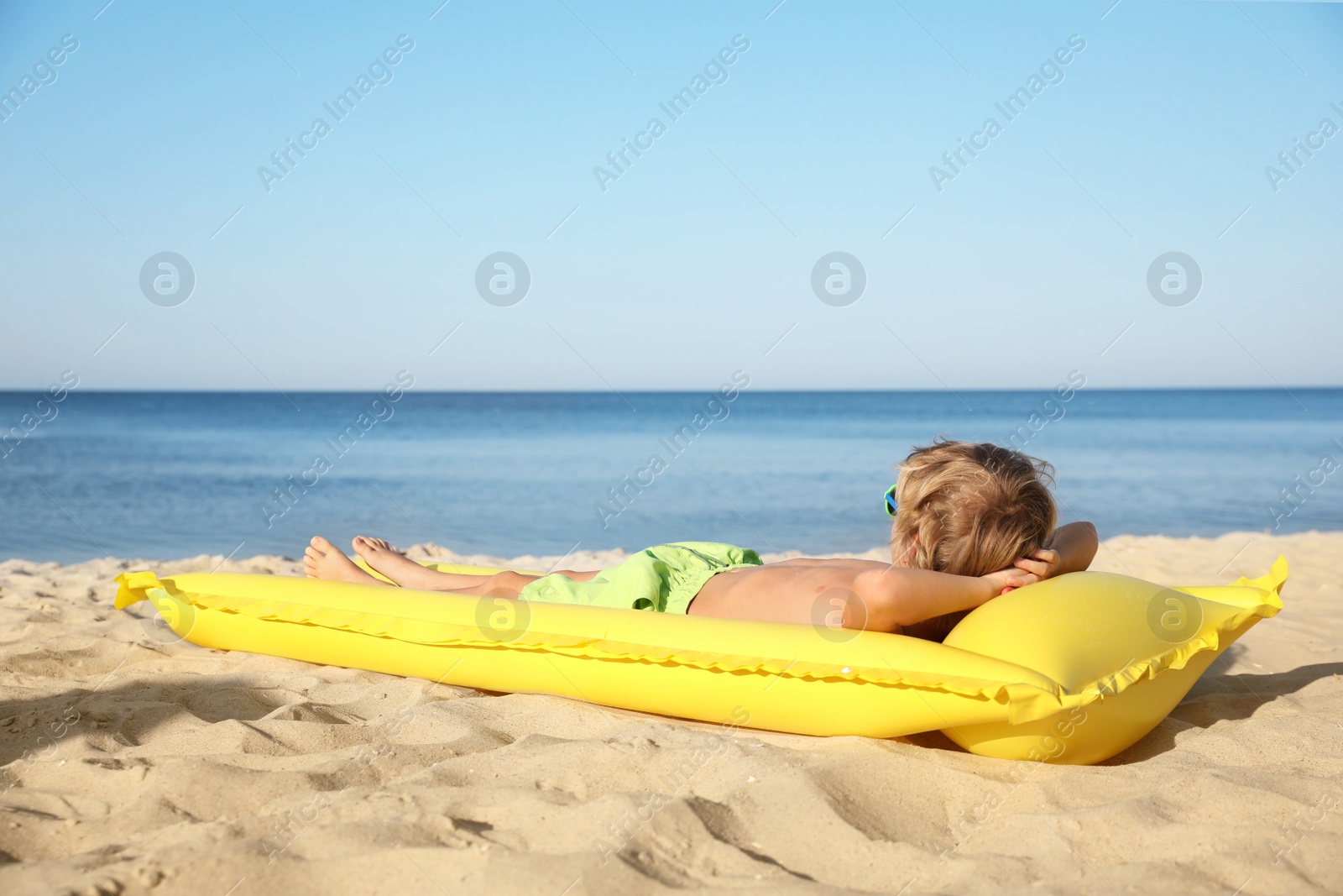 Photo of Cute little child with inflatable mattress lying at sandy beach on sunny day
