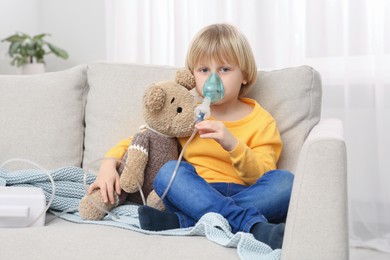 Boy with toy bear using nebulizer for inhalation at home