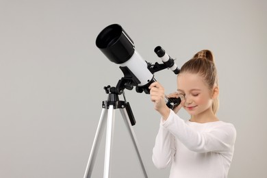 Photo of Little girl looking at stars through telescope on light grey background, space for text
