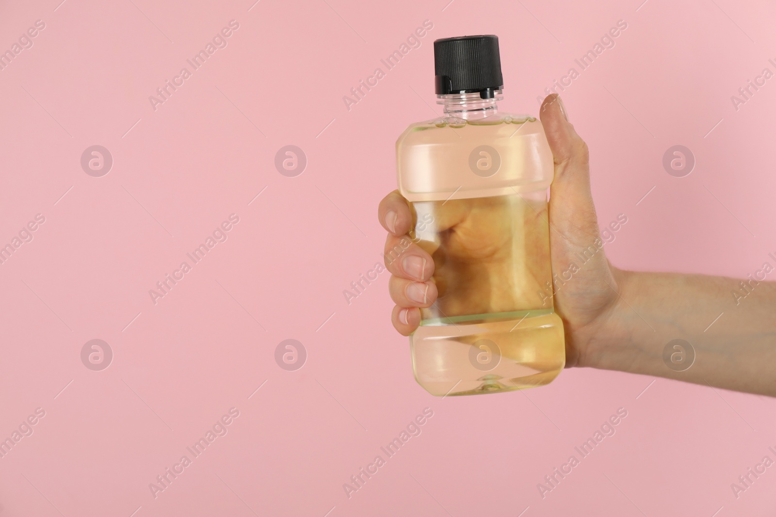 Photo of Woman holding bottle with mouthwash on pink background, closeup. Space for text