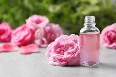 Photo of Bottle of rose essential oil and fresh flowers on table, space for text