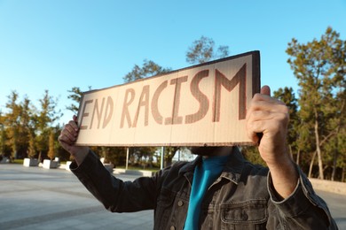 Photo of Young man holding sign with phrase End Racism outdoors