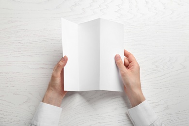 Photo of Young woman holding blank brochure at white wooden table, top view. Mock up for design