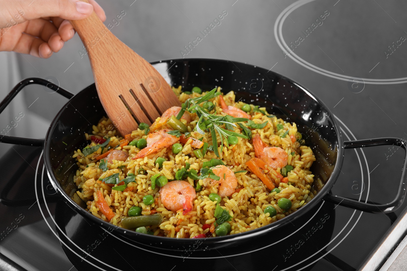 Photo of Woman cooking tasty rice with shrimps and vegetables on induction stove, closeup