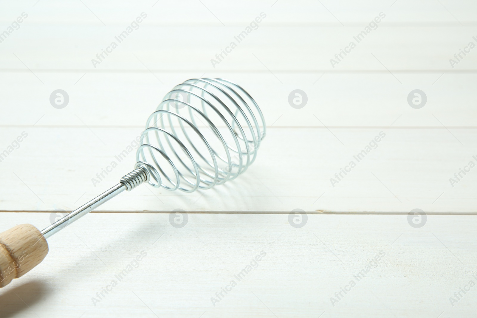 Photo of Metal spring whisk on white wooden table, closeup. Space for text