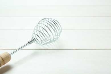 Metal spring whisk on white wooden table, closeup. Space for text