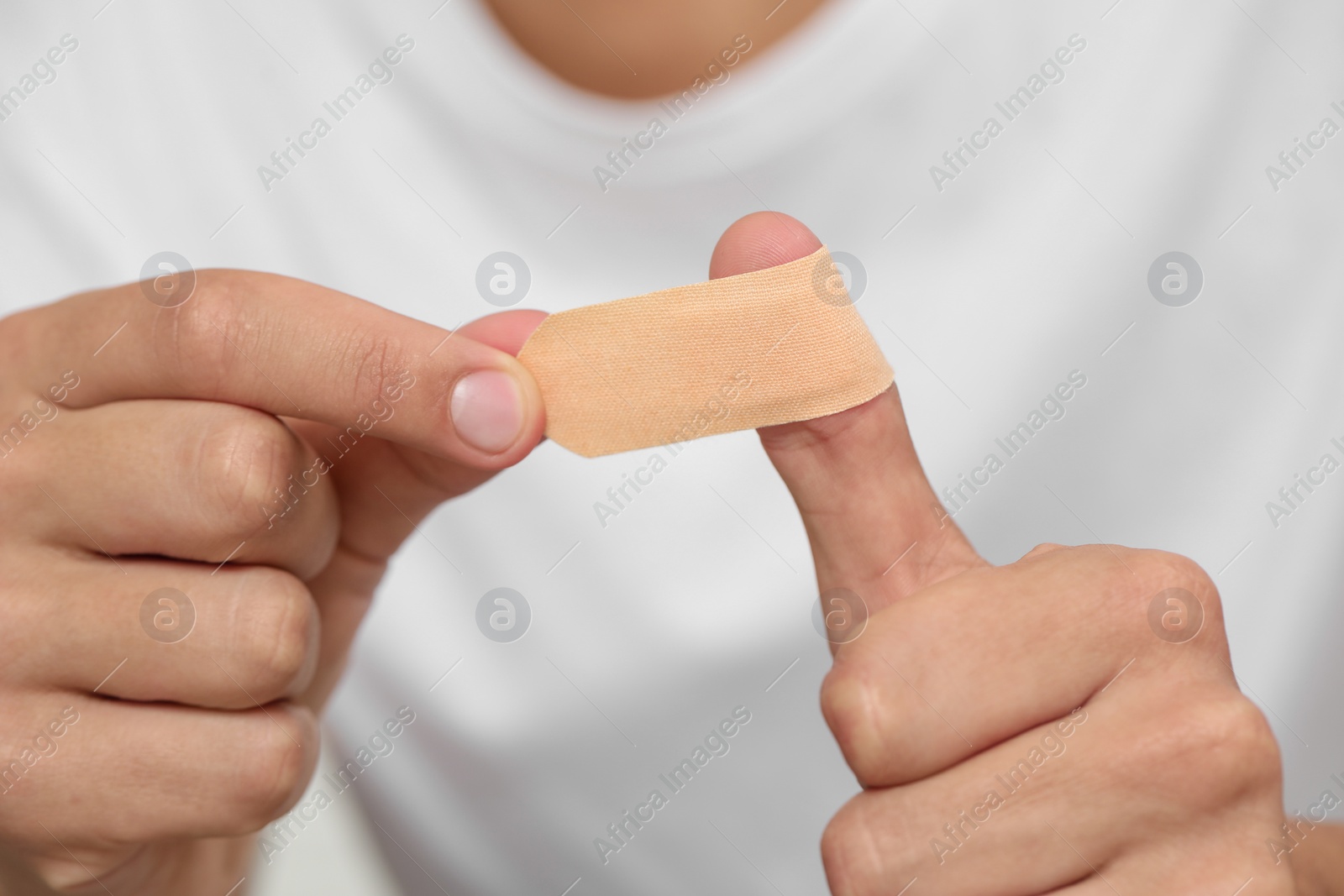 Photo of Man putting sticking plaster onto thumb, closeup