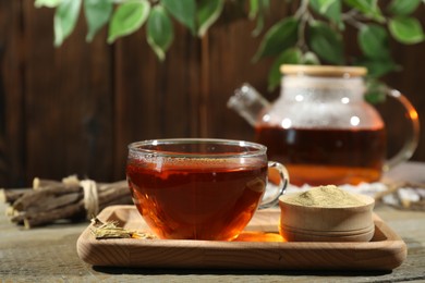 Aromatic licorice tea in cup and powder on wooden table, space for text